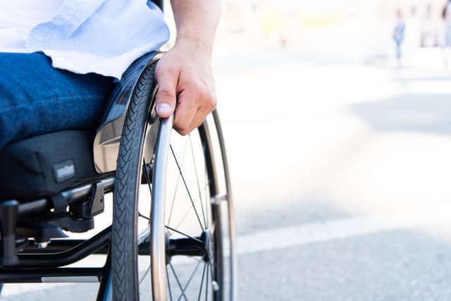 Close-up of a person using a wheelchair outdoors, representing mobility challenges after a catastrophic injury.